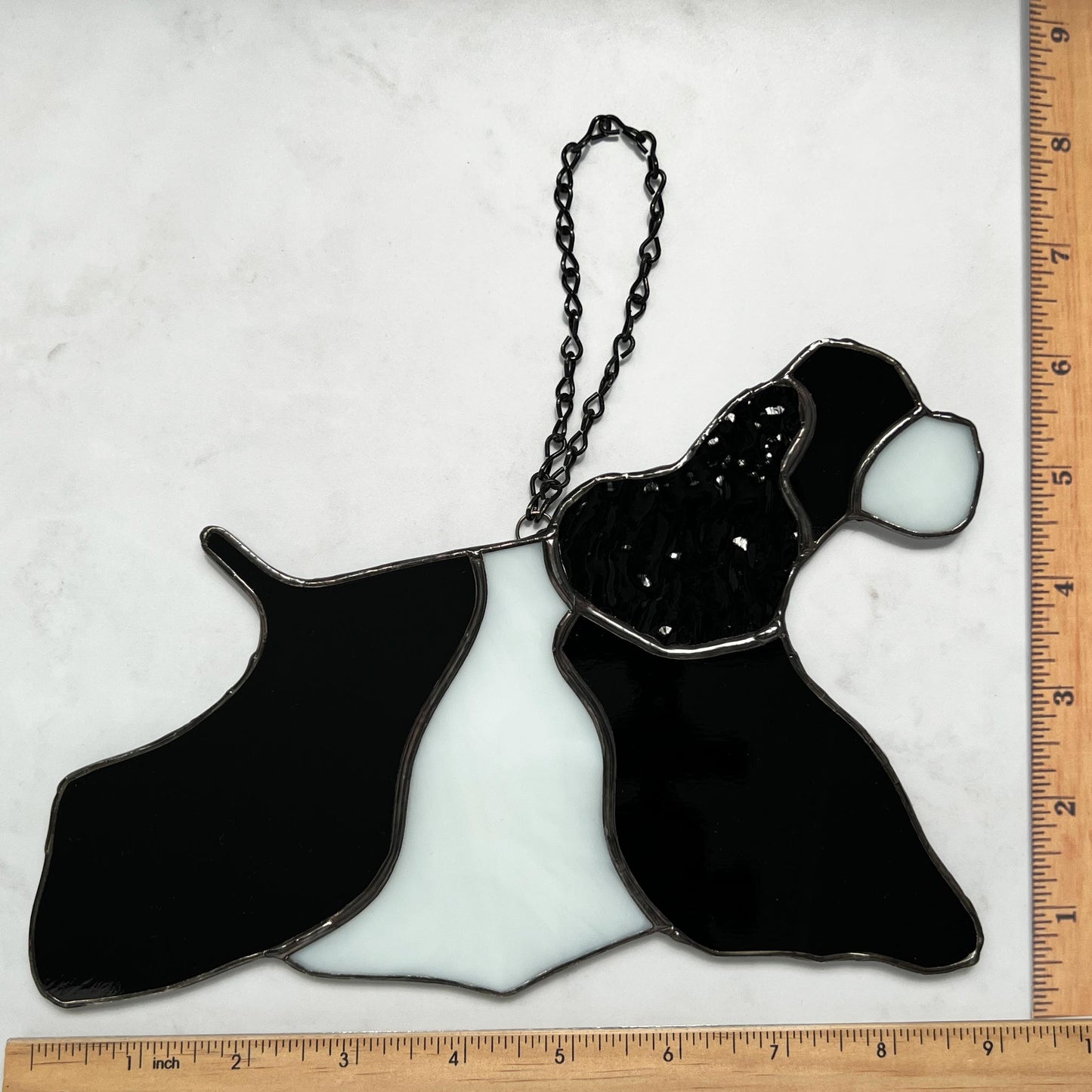 Stained Glass Suncatcher of an American Cocker Spaniel Black and White Parti dog in full competition mode. The ear is made with a rippled black textured glass making it appear realistic. This picture shows the dog with rulers so that you can see it is 9 inches long by 6 inches high