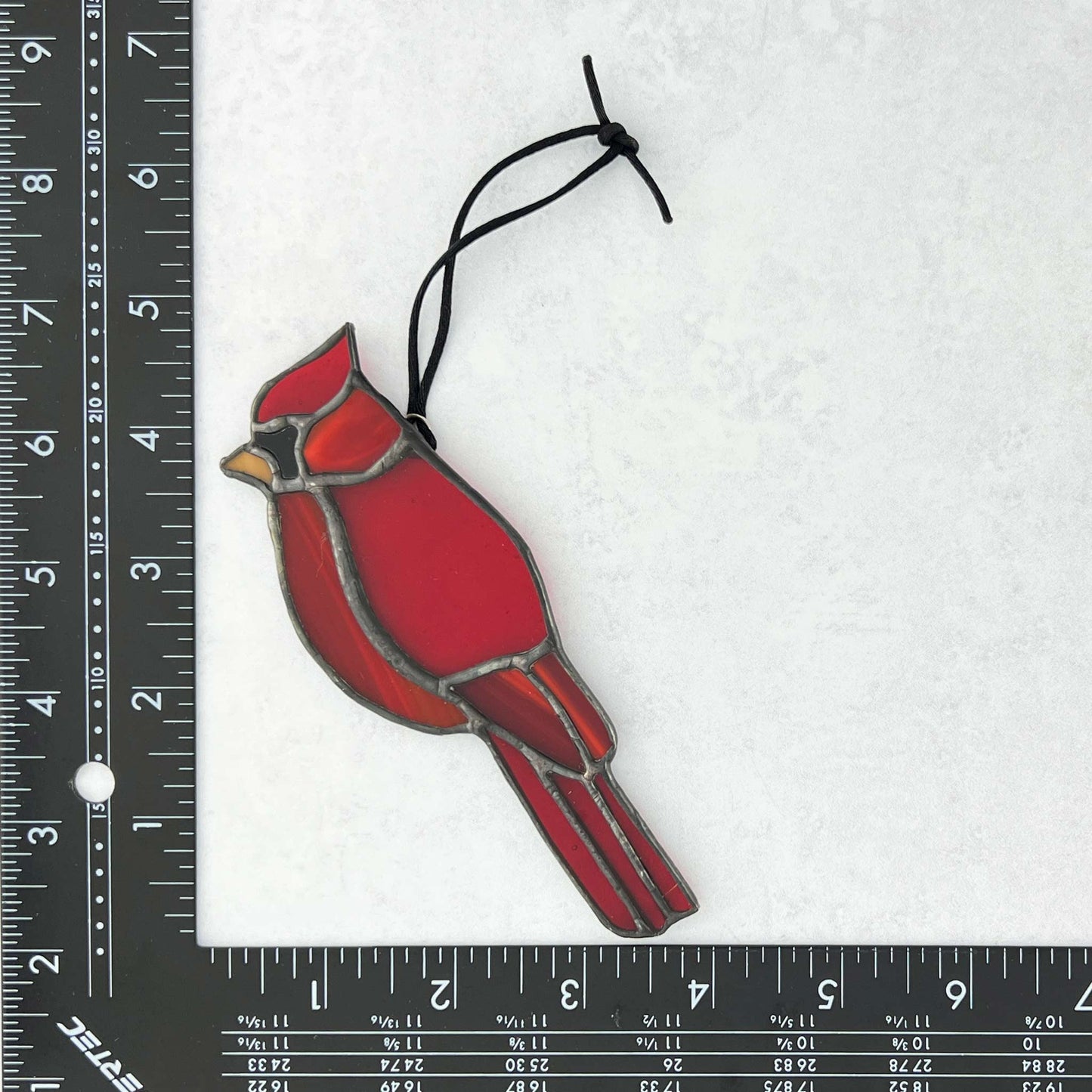 Red cardinal bird ornament with a string on a white background with a ruler for scale.
