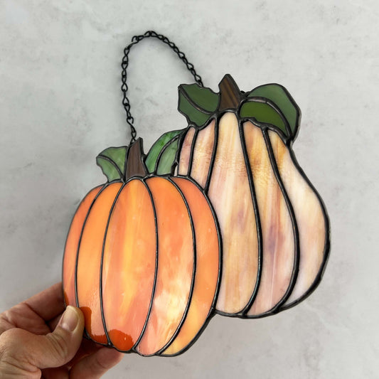 Hand holding an orange pumpkin and light orange-amber gourd suncatcher with 4 green leaves and a metal chain