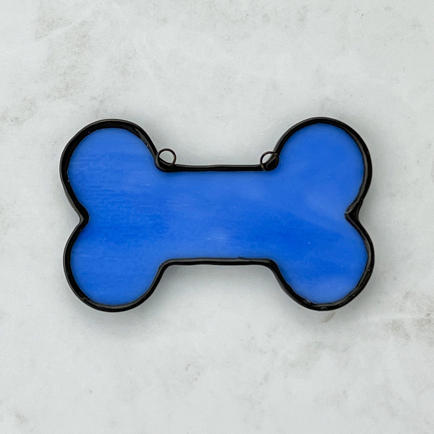 The back of a spotted blue stained glass dog bone suncatcher ornament. The back is a solid sky blue color.