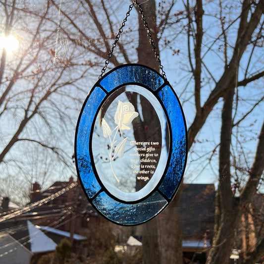 This stained glass beveled oval suncatcher with an etched rose is a beautiful piece that makes a perfect gift for any mother. It measured 8x6 inches and the bevel is surrounded by an inch of multicolored blue glass. This suncatcher is an ideal gift for any occasion when you express your appreciation to your mother.