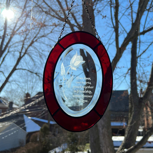 This suncatcher has an etched rose and the etched saying "Two lives, two hearts, joined together in friendship, united forever in love," making it a perfect gift for the couple who was recently married, engaged, or who are celebrating an anniversary. The piece measures 8x6 inches. The bevel is surrounded by red glass.