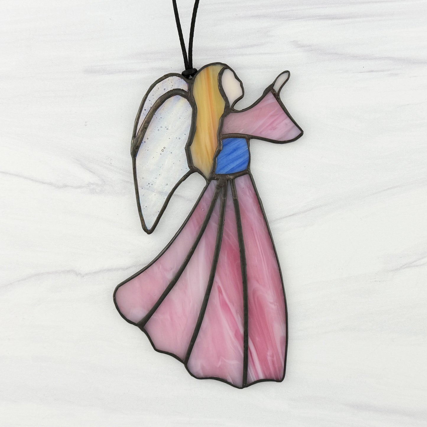 Stained glass angel suncatcher with a Pink dress and sleeve, Blue bodice, golden hair, and Iridescent clear wings. Shown on  white background facing right.