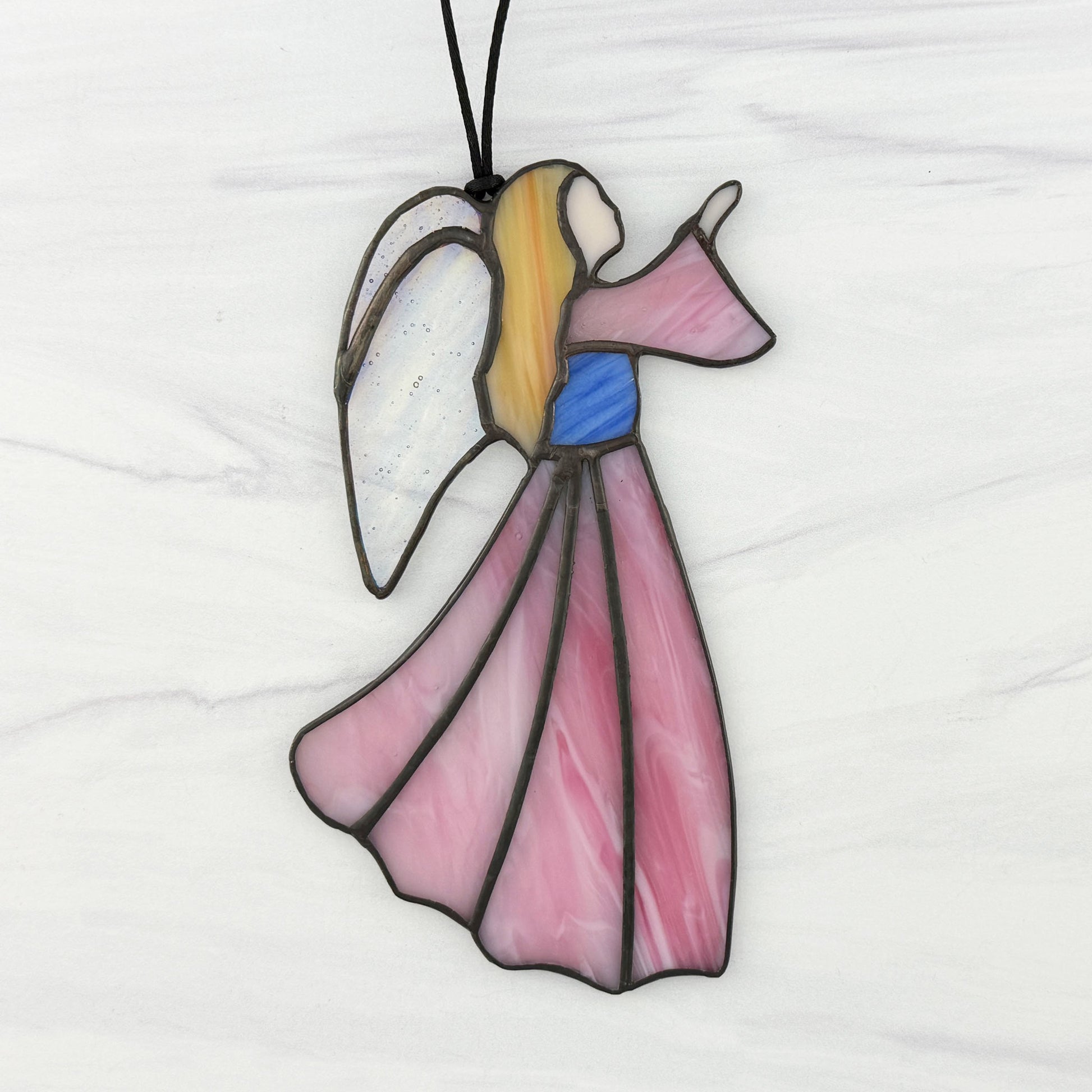 Stained glass angel suncatcher with a Pink dress and sleeve, Blue bodice, golden hair, and Iridescent clear wings. Shown on  white background facing right.