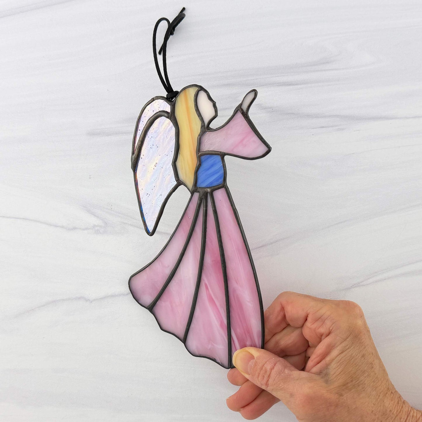 Stained glass angel ornament held by a hand against a white background