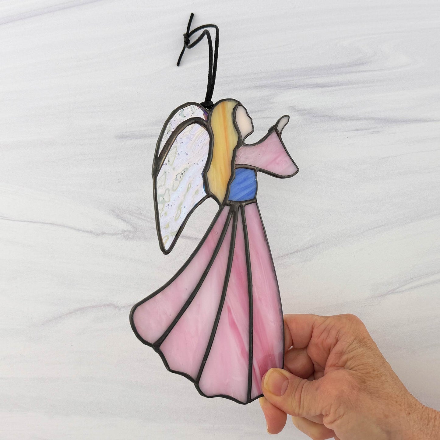 Hand holding a stained glass angel decoration against a white background.