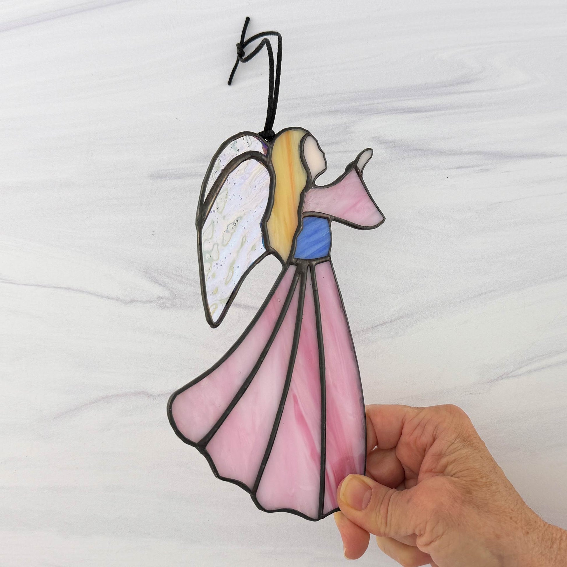 Hand holding a stained glass angel decoration against a white background.