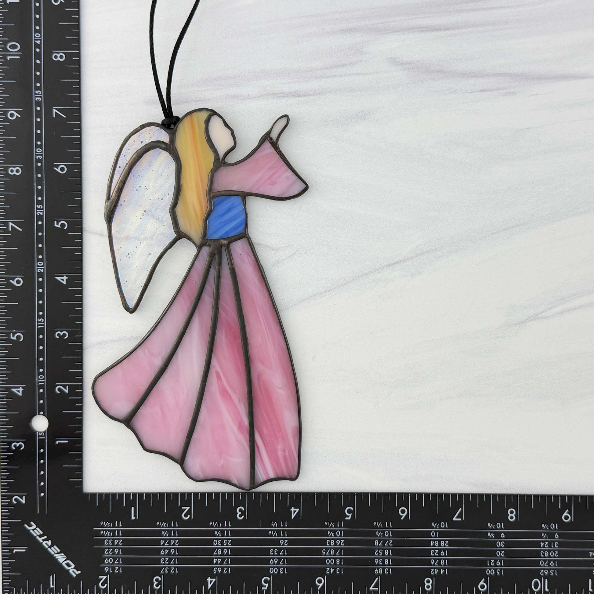 Pink stained glass angel suncatcher with a ruler for scale on a white background
