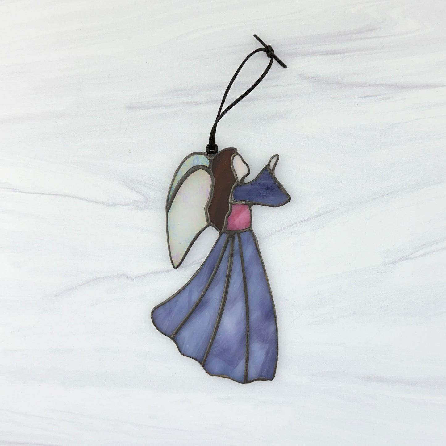 Stained glass angel ornament on a white background. She has a purple dress and sleeve, pink bodice, brown hair and irridescent white wings. Her hand is raised to the right.