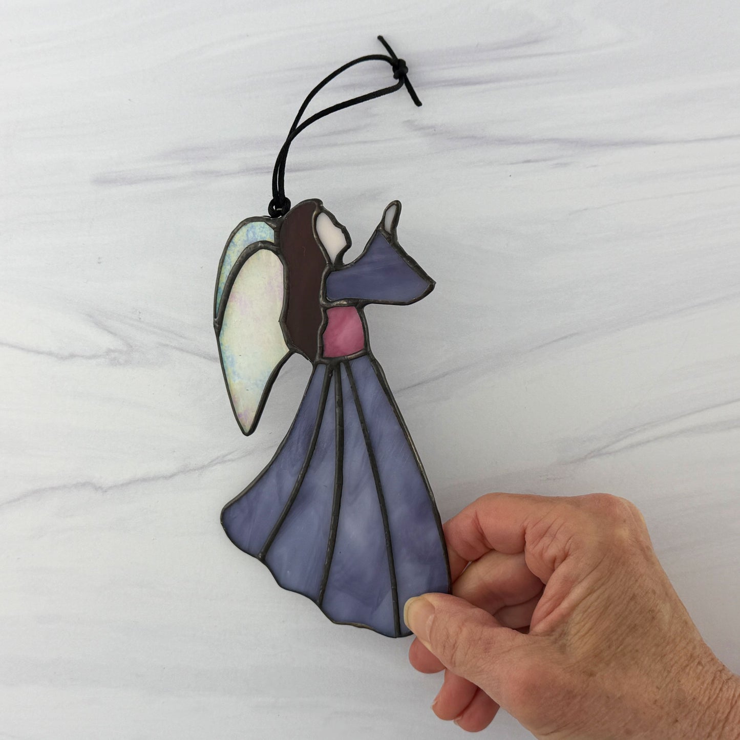 Purple stained glass angel ornament held by a hand against a white background