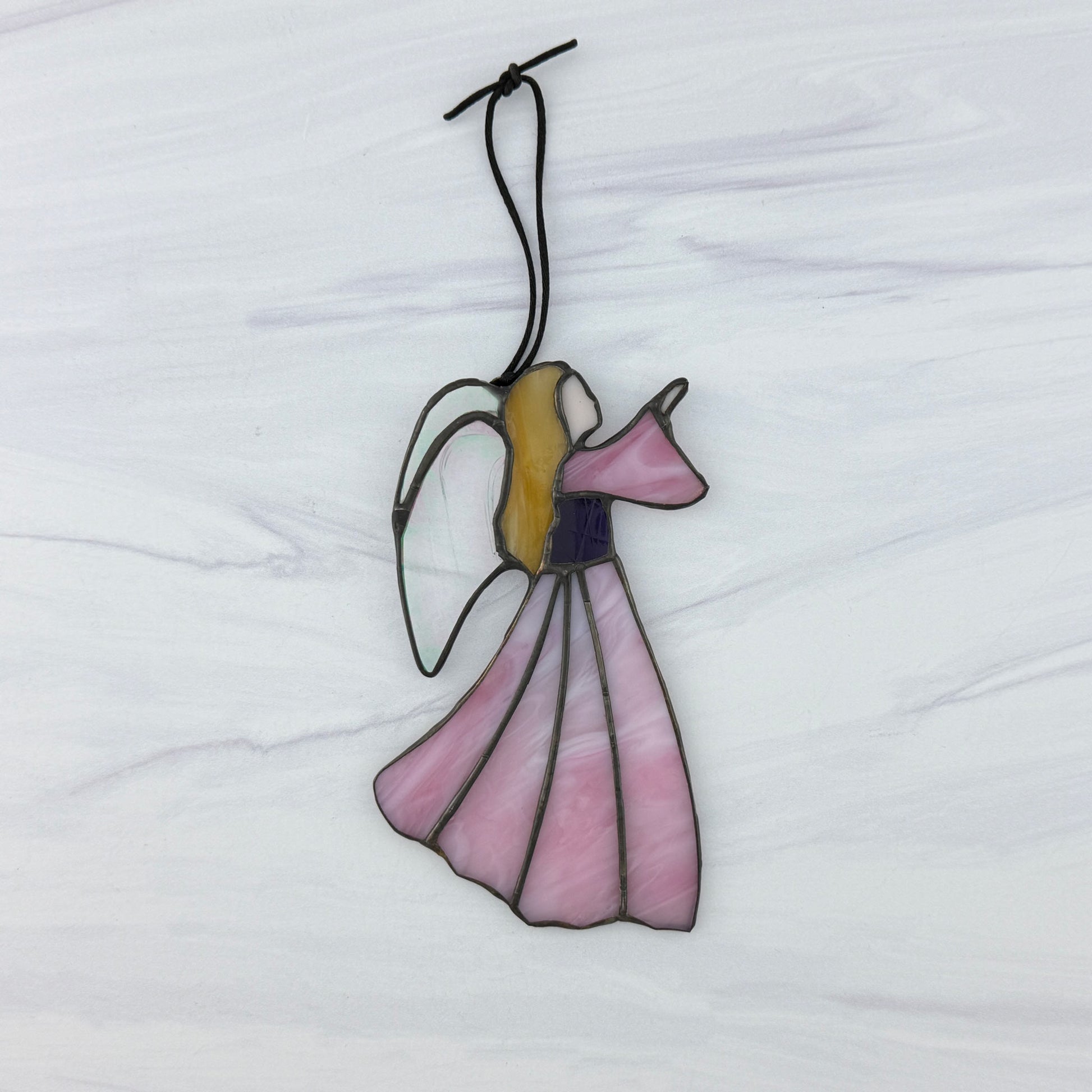 Pink stained glass angel ornament on a white background. She has a purple bodice, golden hair, pink sleeve and clear irridescent wings. A black cord for hanging too.