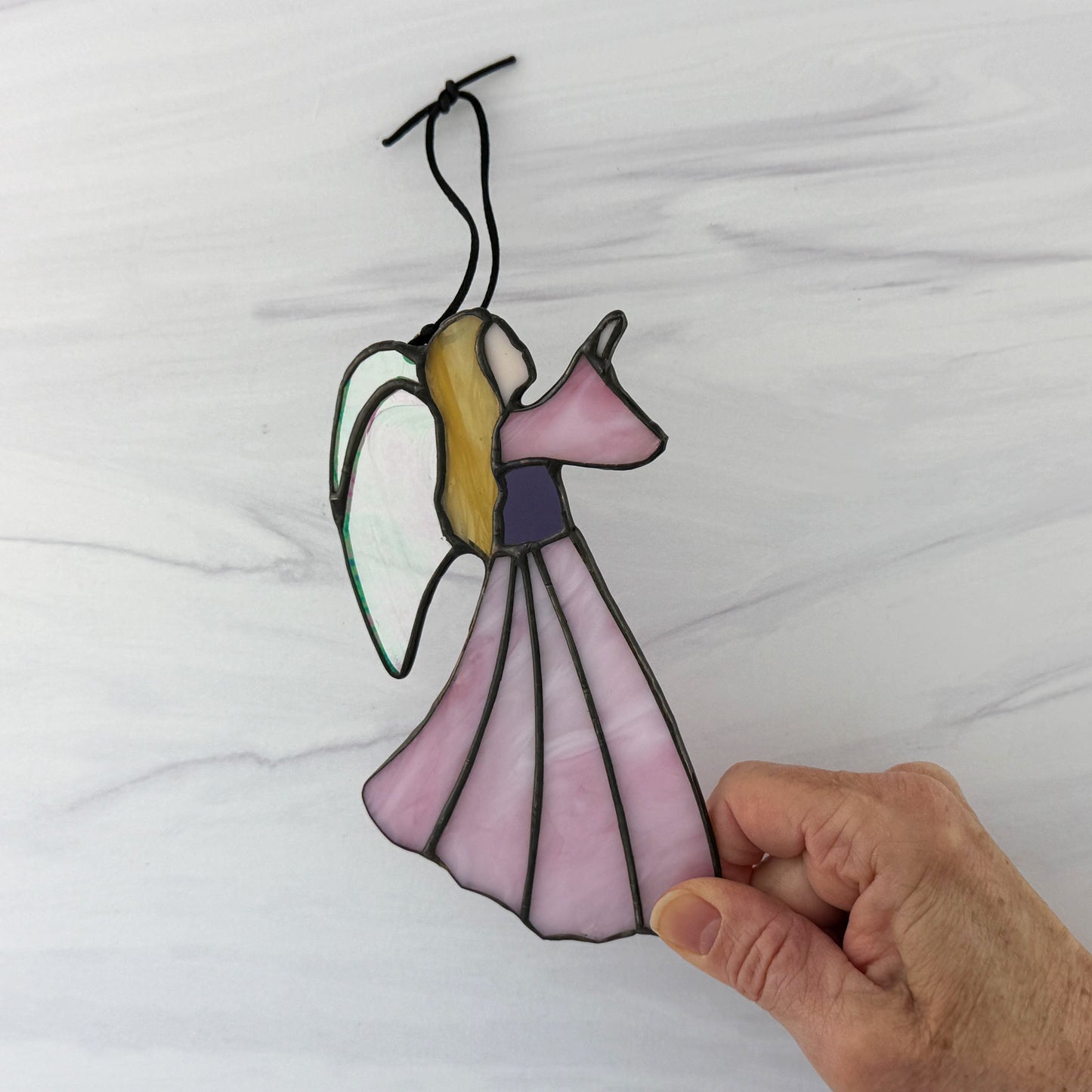 Stained glass angel hanging ornament held by a hand against a white background