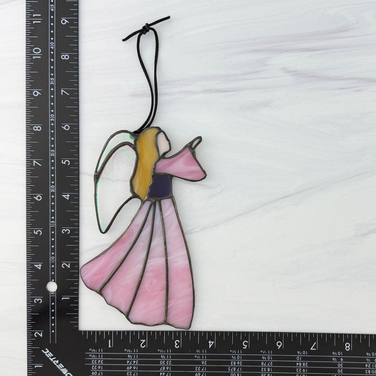 Stained glass angel with pink dress displayed on a white background with a ruler for scale.