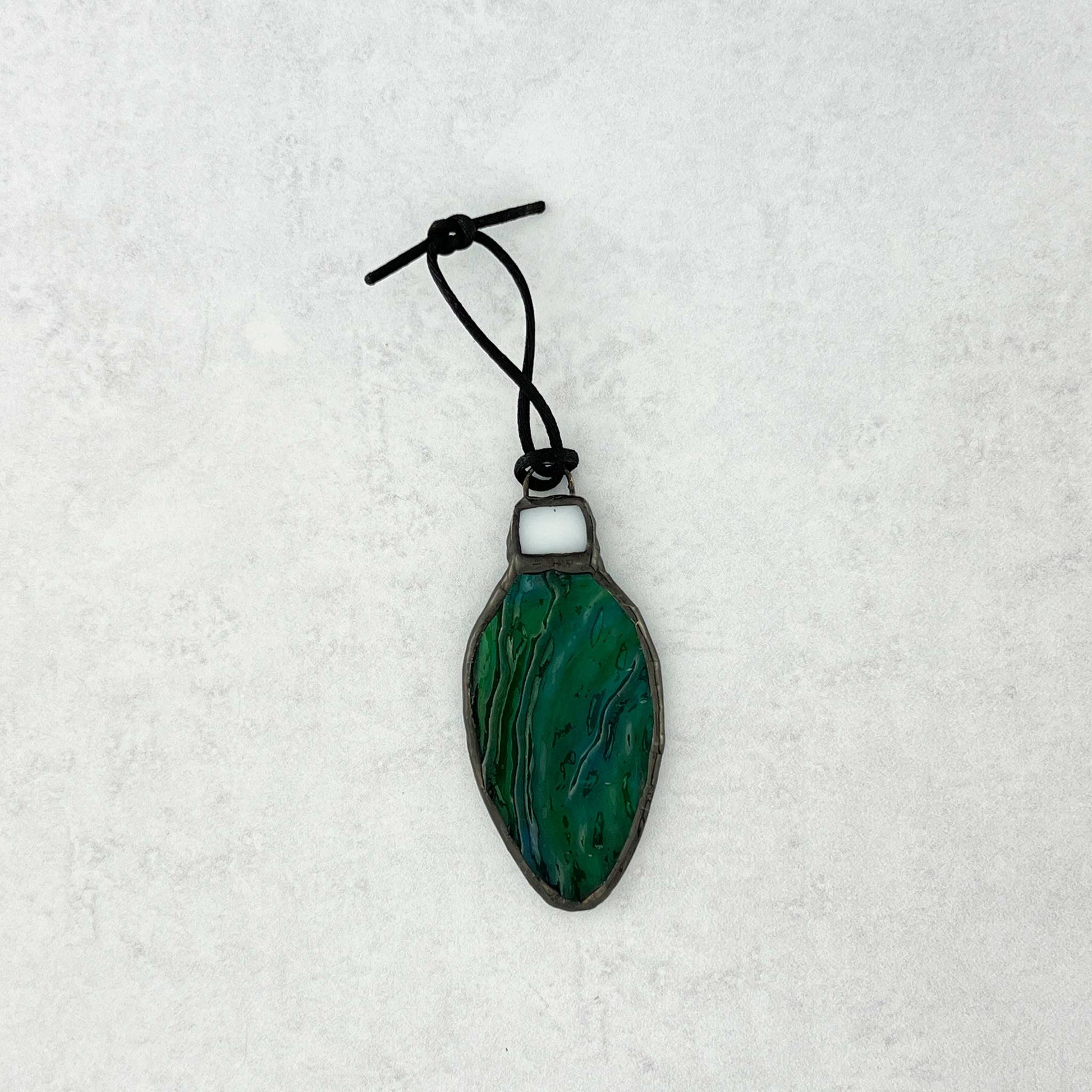 Green-Blue rippled stained glass bulb shaped Christmas ornament hung from a black cord shown on a white background.