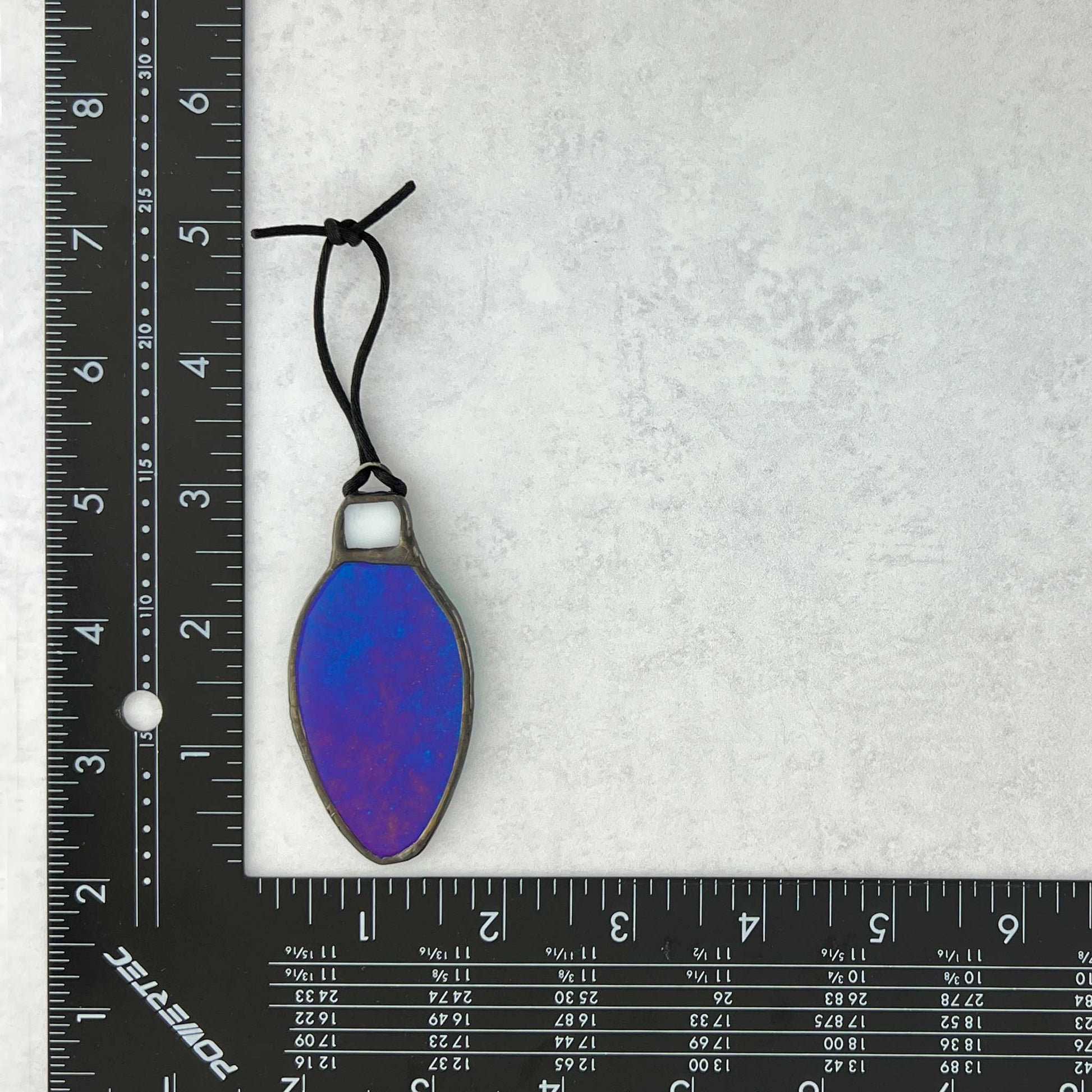 Iridescent Teal-Blue stained glass bulb shaped Christmas ornament shown with a ruler for size reference