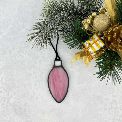 Pink and white stained glass bulb shaped Christmas ornament hung from a black cord.  Shown on a christmas tree branch.