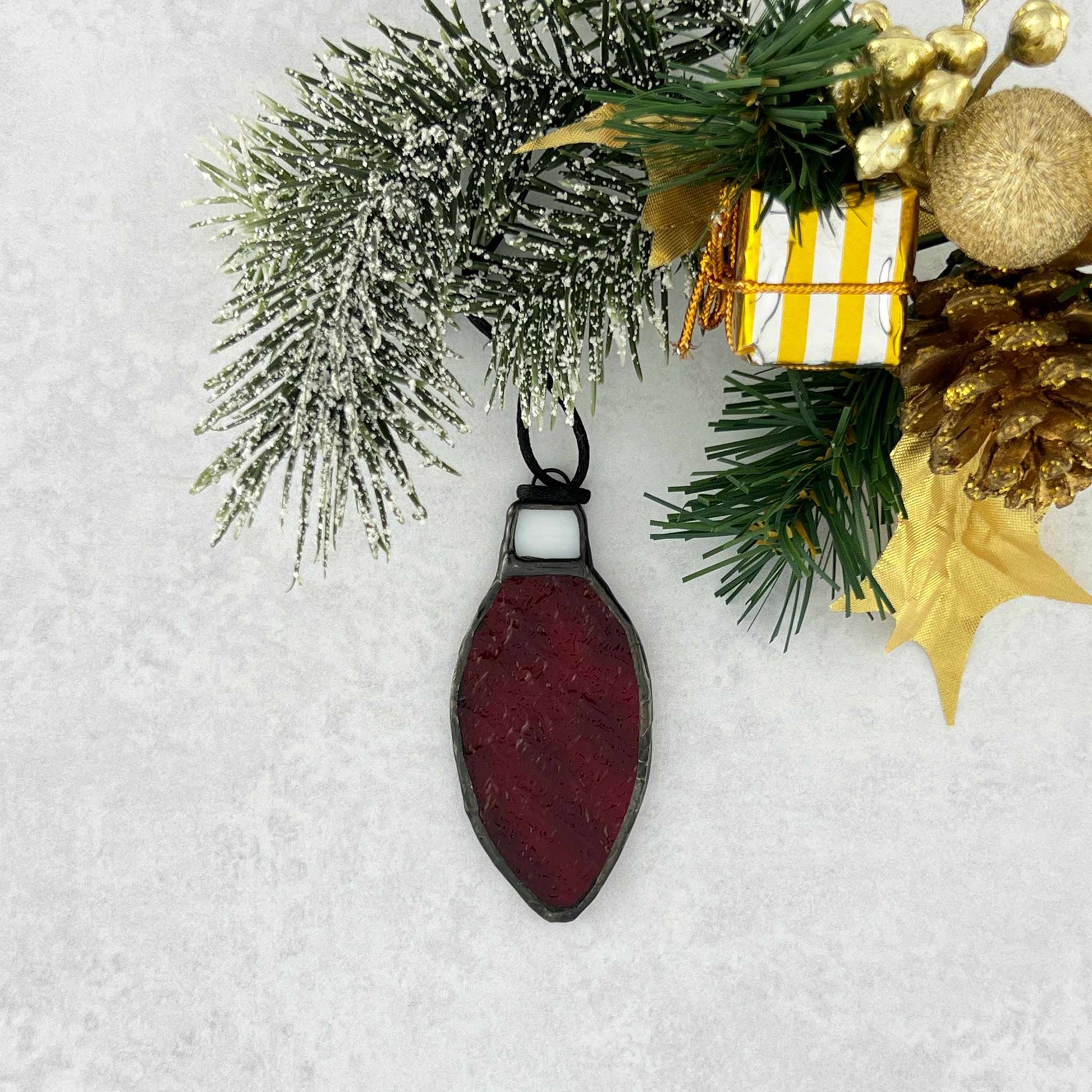 Red rippled stained glass bulb shaped Christmas ornament hung from a black cord.  Shown hanging from a christmas tree branch.