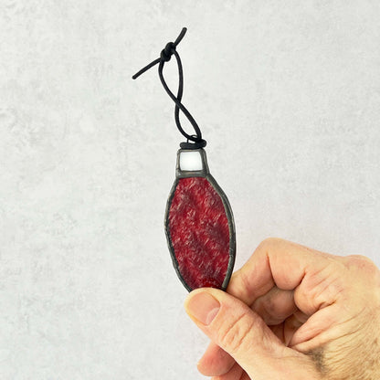 Hand holding a Red rippled stained glass bulb shaped Christmas ornament hung from a black cord. 