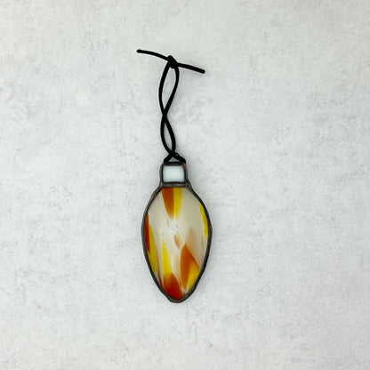 Decorative yellow-orange-white and clear stained glass bulb shapped ornament on a black string shown on a white background