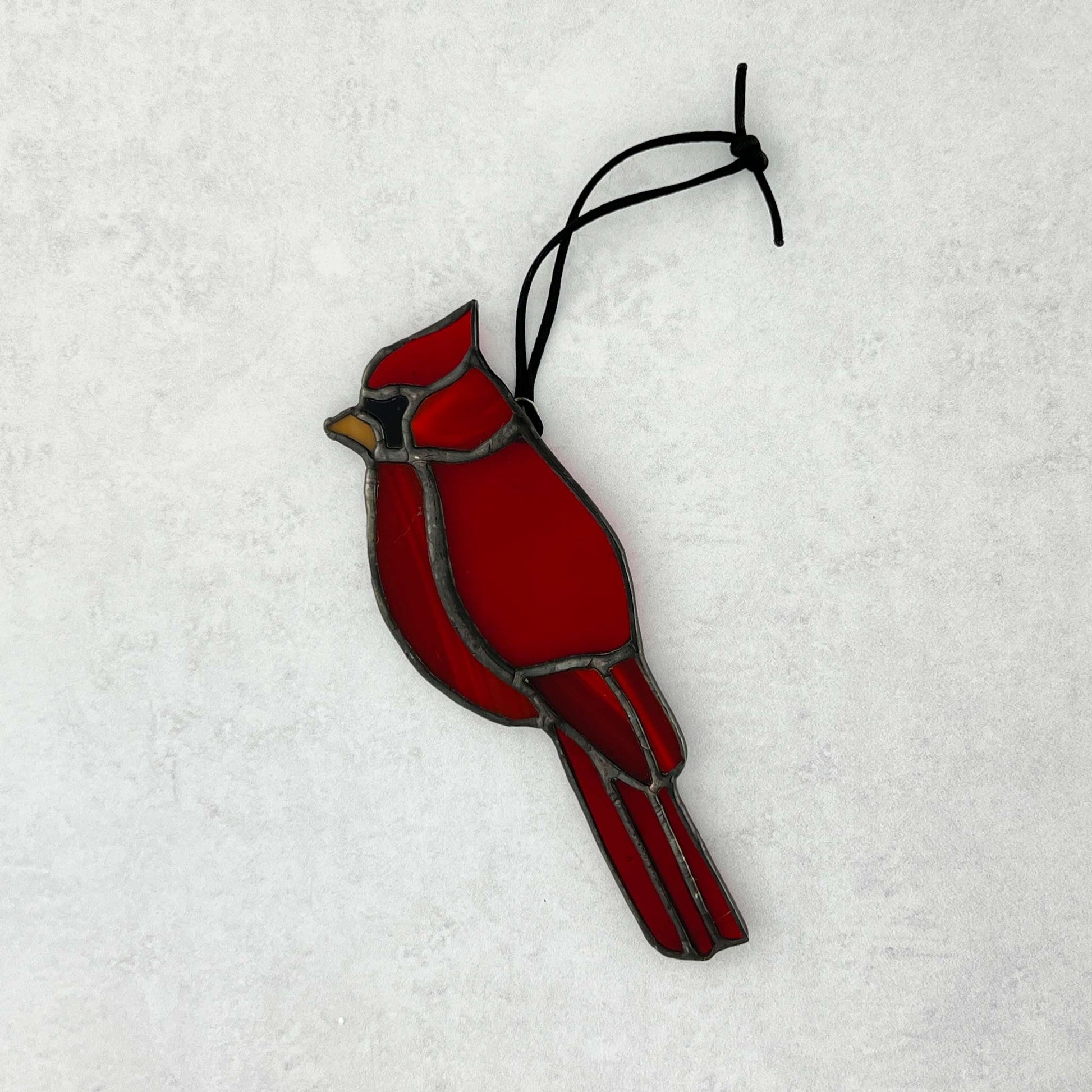 Red stained glass cardinal bird ornament on a white background. Various colors of red glass are used with an orange beak and a black cord for hanging.
