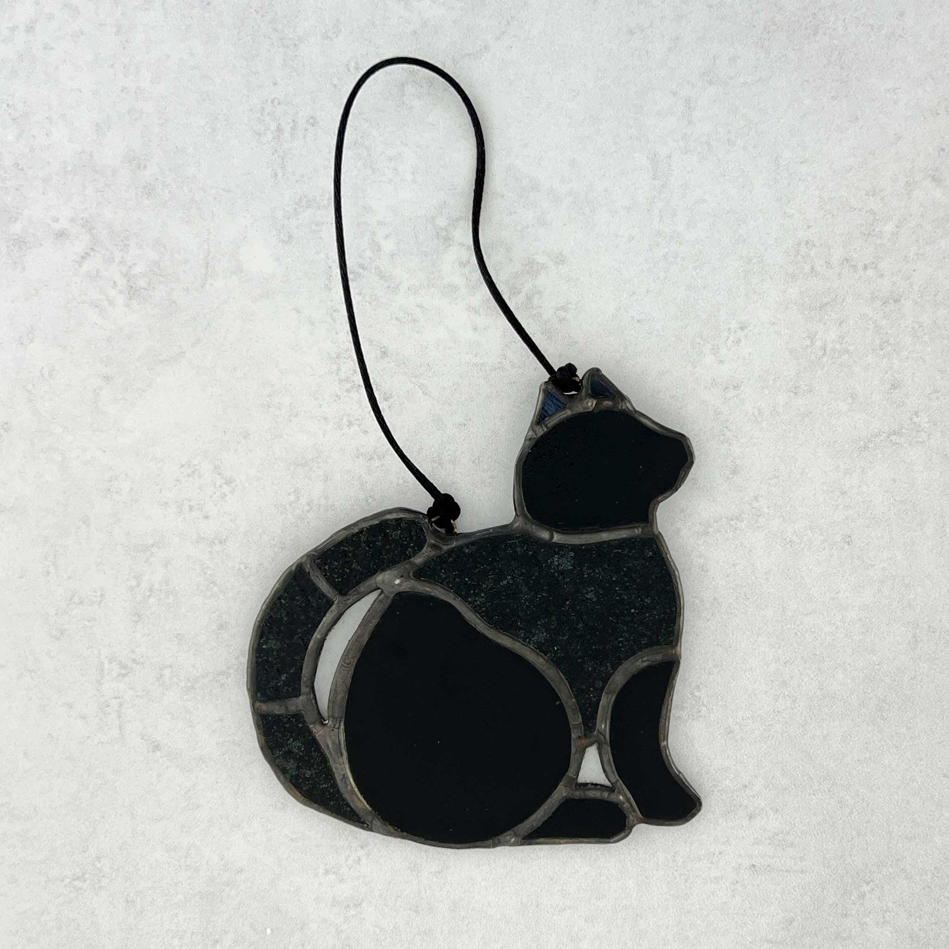 Stained glass Black cat ornament made of smooth and textured black glass. Black cord for hanging is shown.