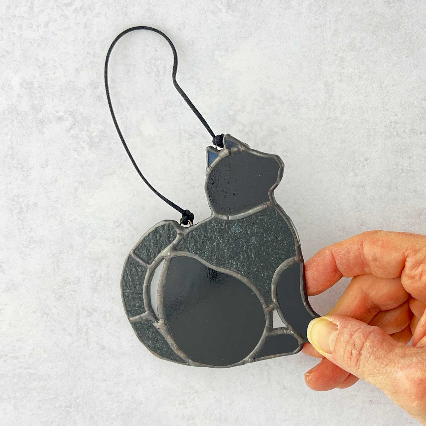 Hand holding a stained glass Black cat ornament made of smooth and textured black glass. 