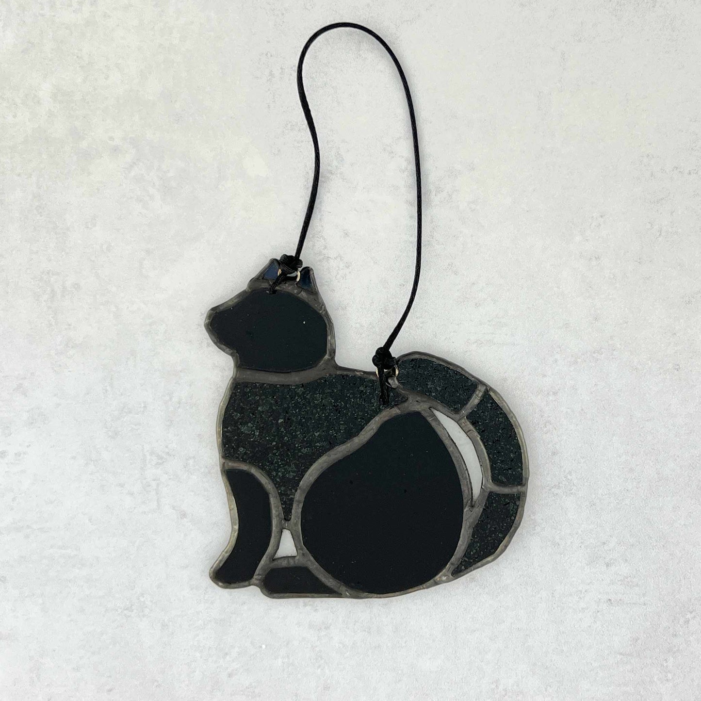 The back side of a stained glass Black cat ornament made of smooth and textured black glass. 