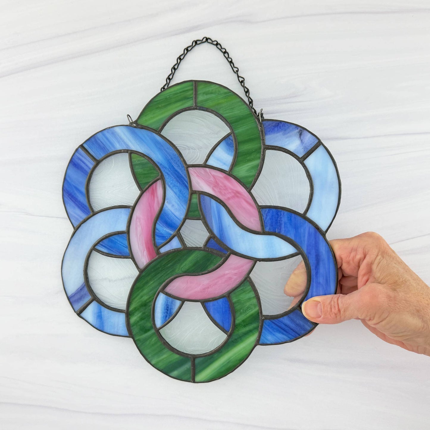 Stained glass panel with Celtic knot design held by a hand against a white background