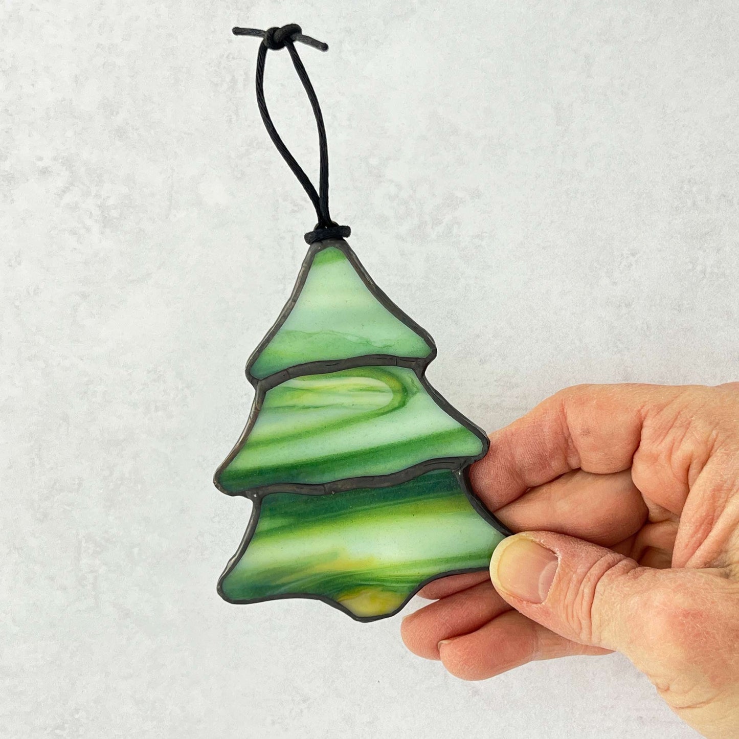 Hand holding a green glass Christmas tree ornament against a white background
