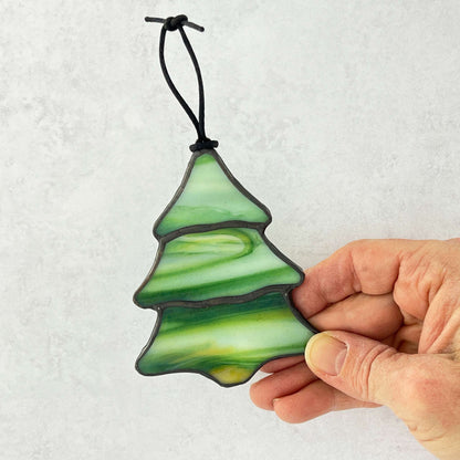 Hand holding a green glass Christmas tree ornament against a white background