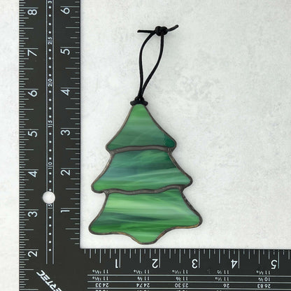 Green stained glass Christmas tree ornament next to a ruler on a white background