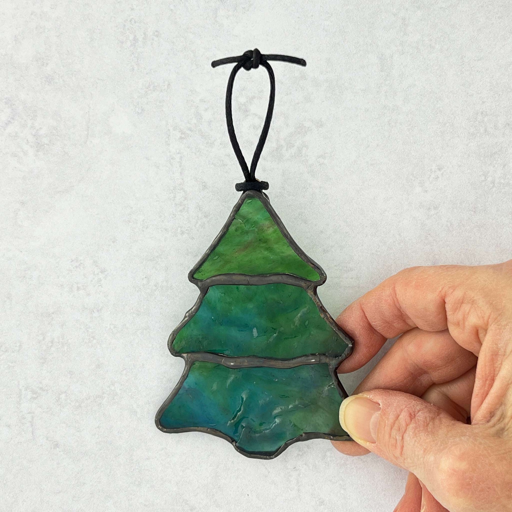 Hand holding a blue-green stained glass Christmas Tree made with a ripple textured glass