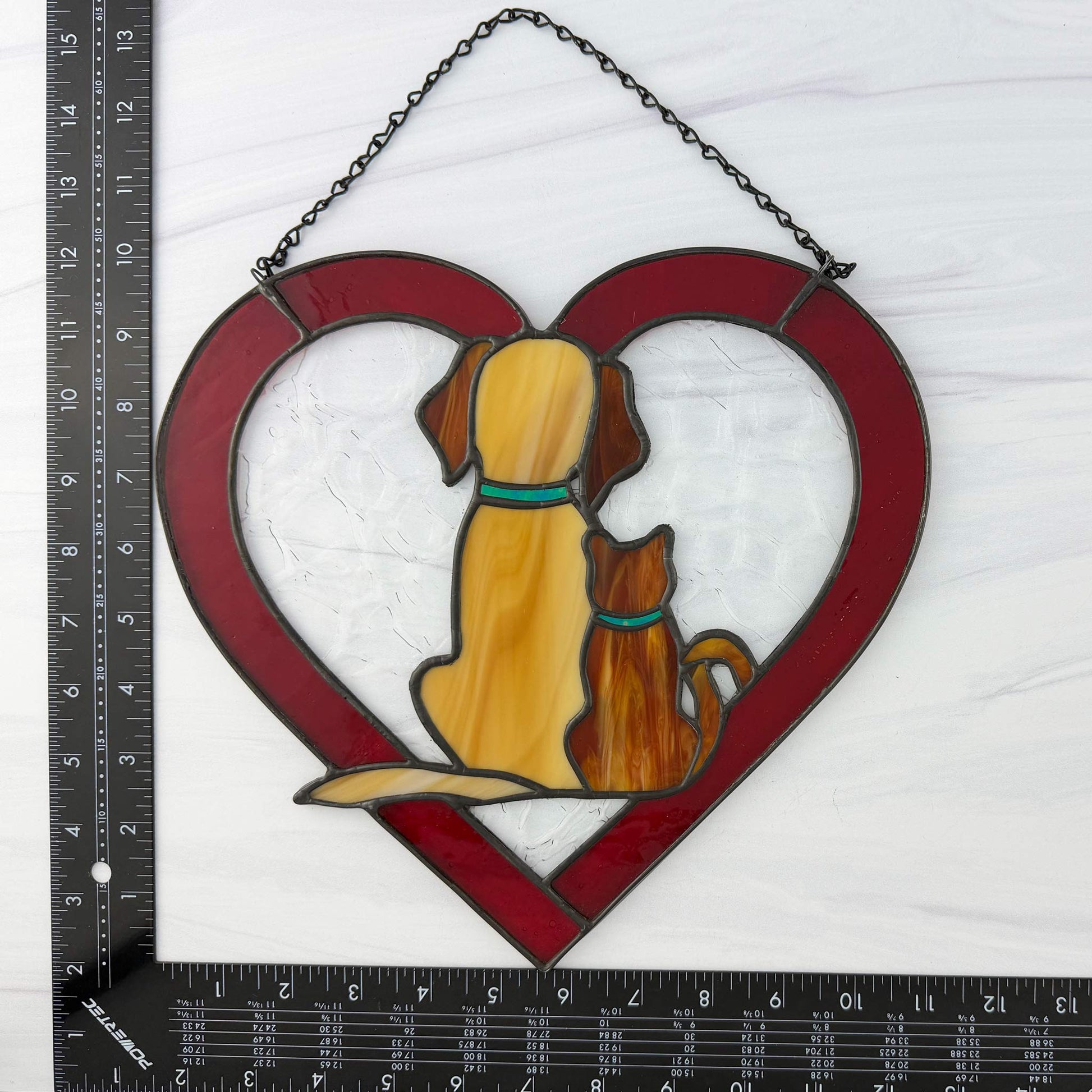 Stained glass heart-shaped suncatcher with a dog and cat on a white background. 
Shown with a ruler for scale.