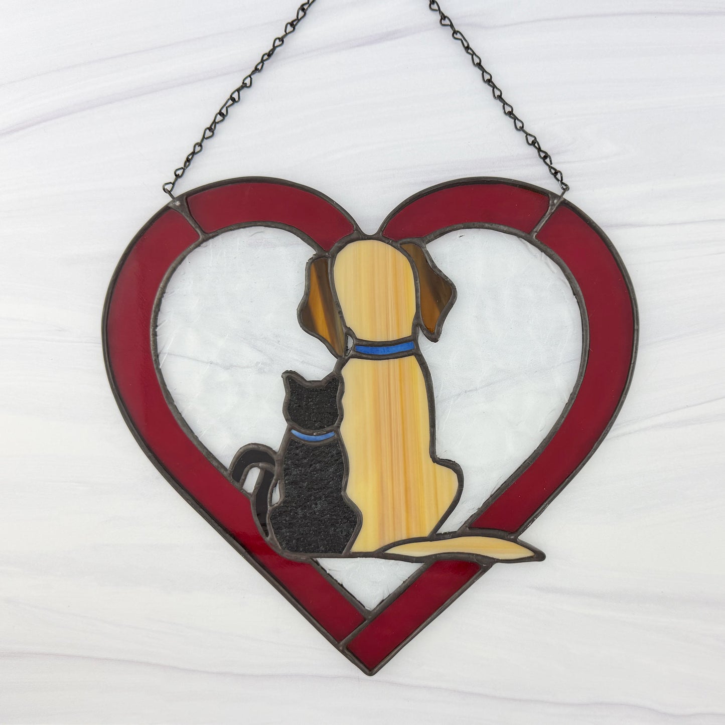 Stained glass red heart-shaped window hanging with a dog and cat sitting together. This is the back view.