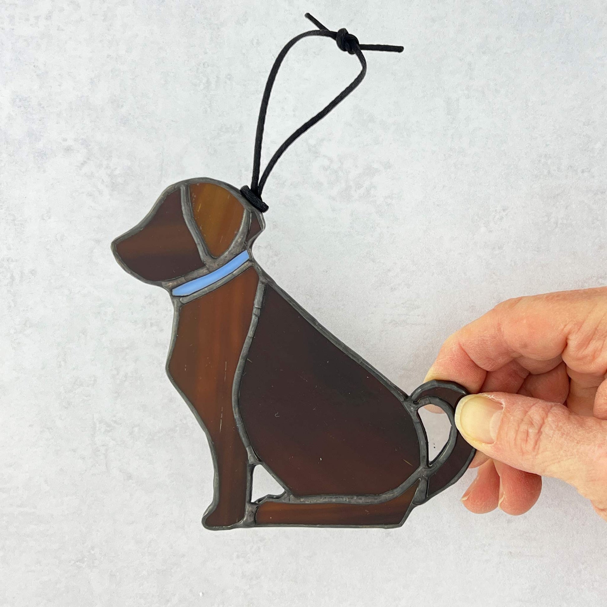 Decorative brown stained glass dog ornament with a hand holding it against a light gray background. 