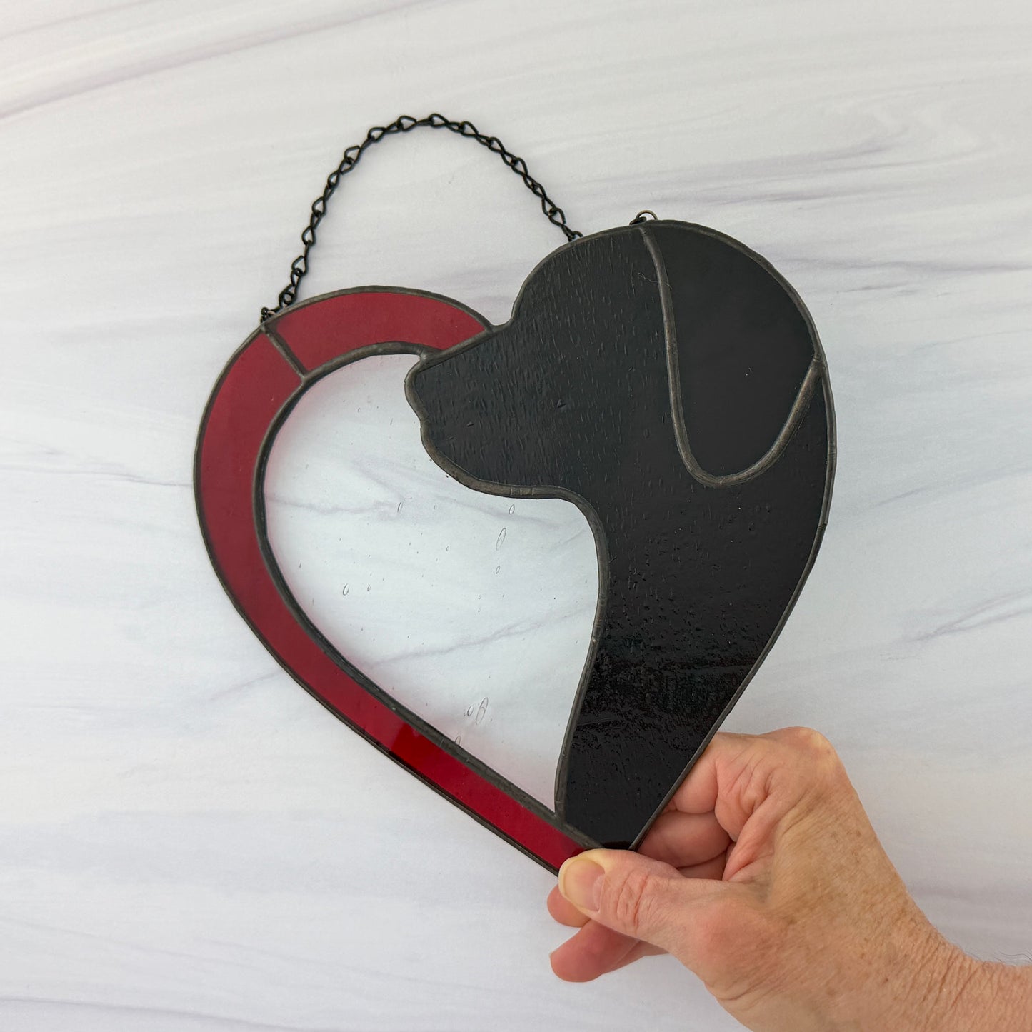 Half a red Heart stained glass suncatcher with a dog silhouette held by a hand on a white background