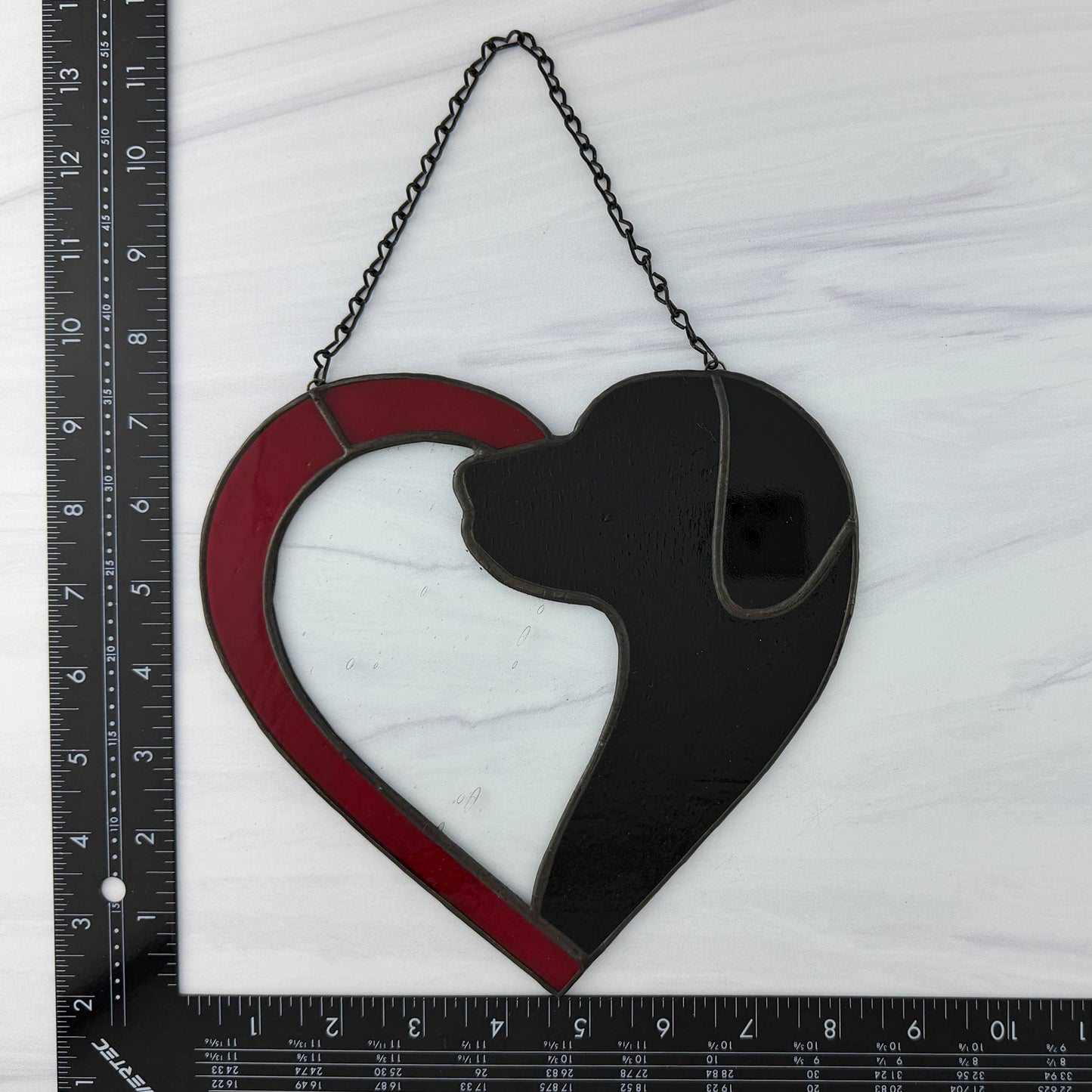 Heart-shaped suncatcher with a black silhouette inside, hanging on a white background with a ruler for scale.