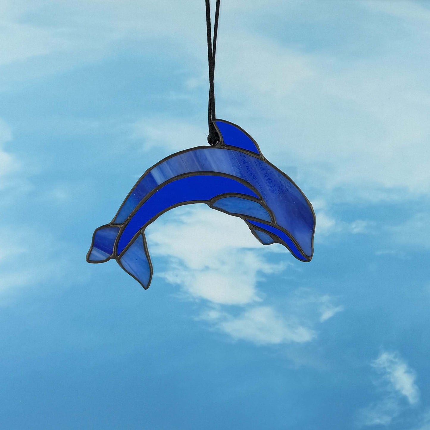 Blue stained glass dolphin hanging against a blue sky with clouds