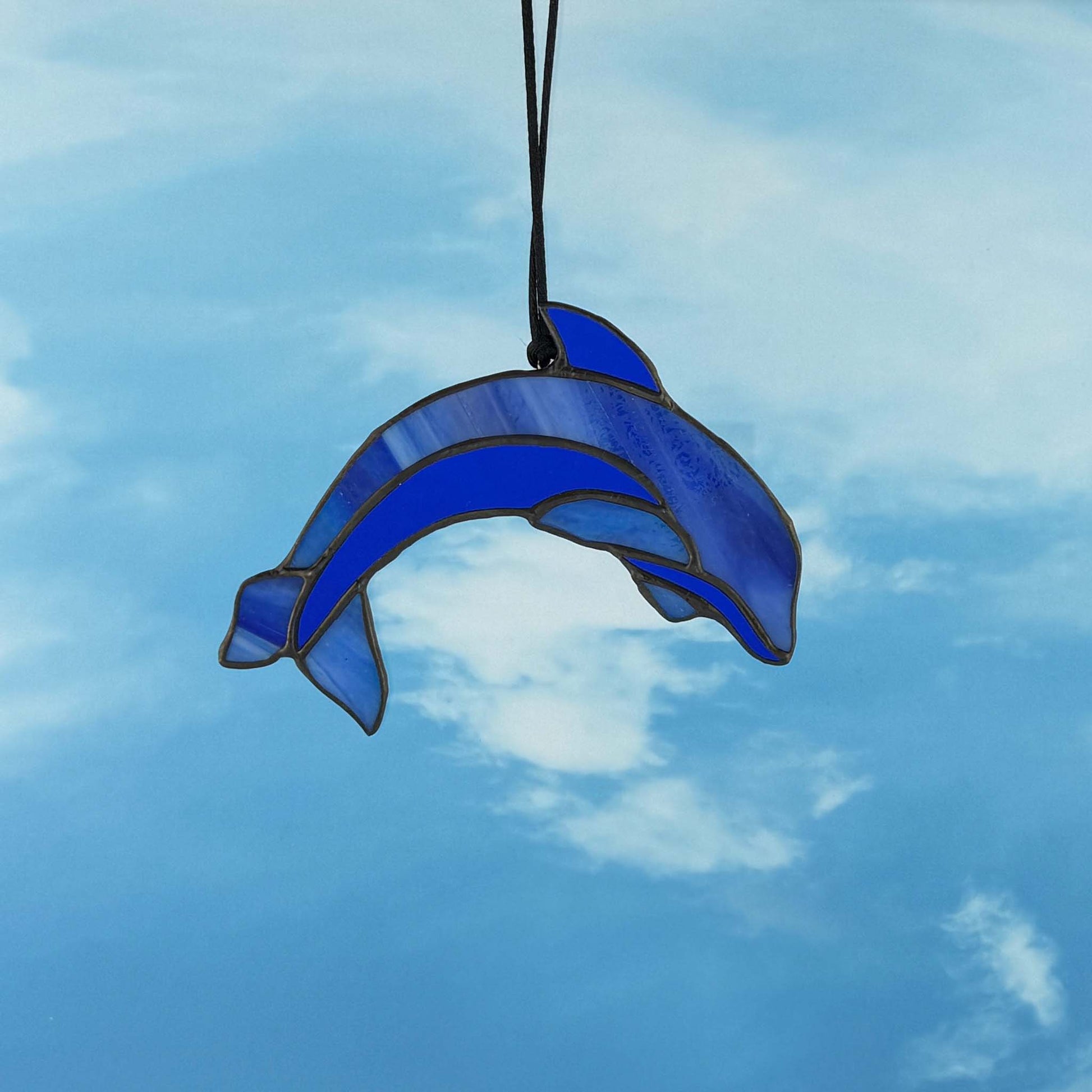 Blue stained glass dolphin hanging against a blue sky with clouds