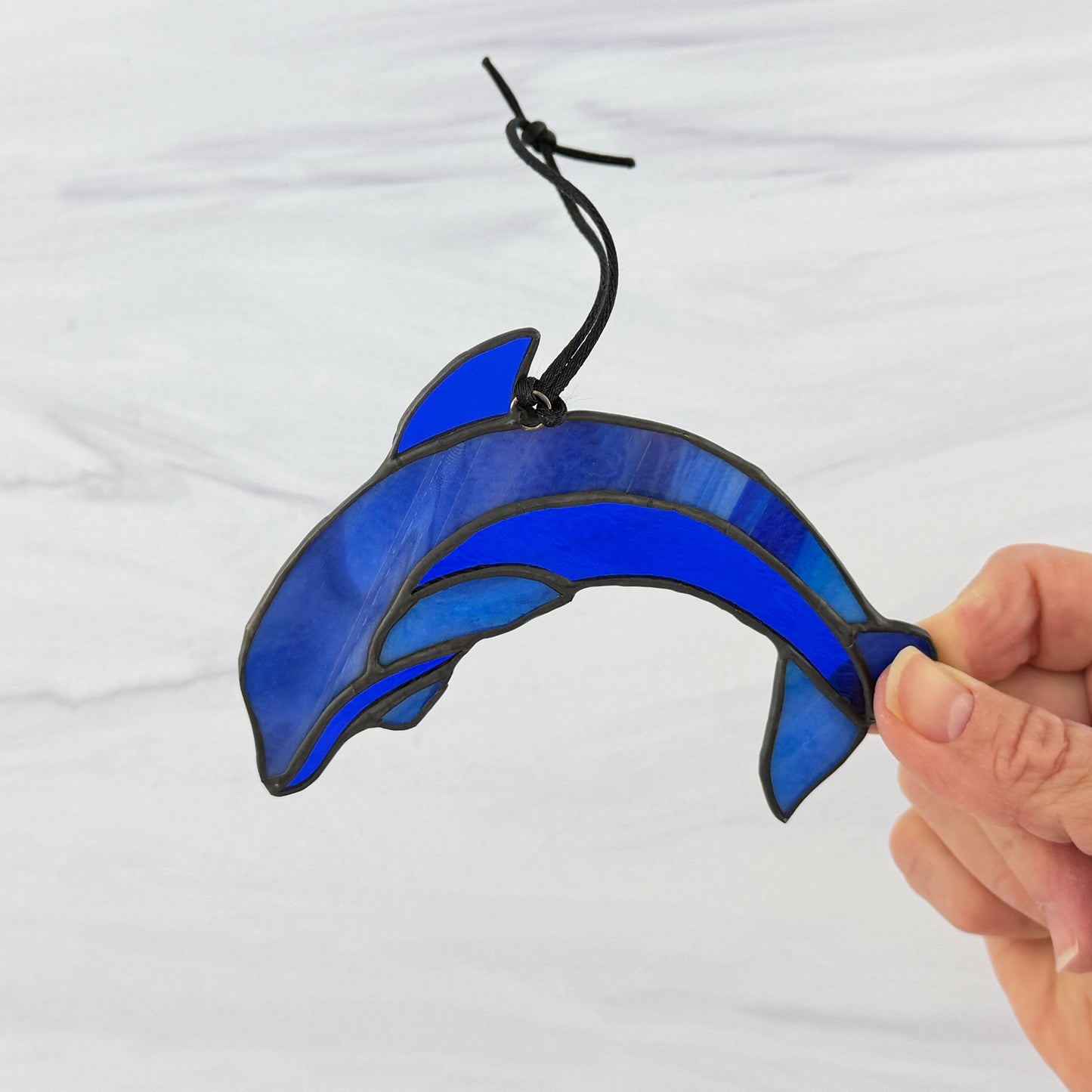 Blue stained glass dolphin ornament held by a hand against a white background
