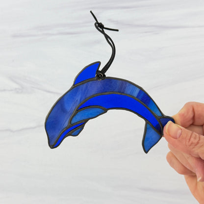 Blue stained glass dolphin ornament held by a hand against a white background