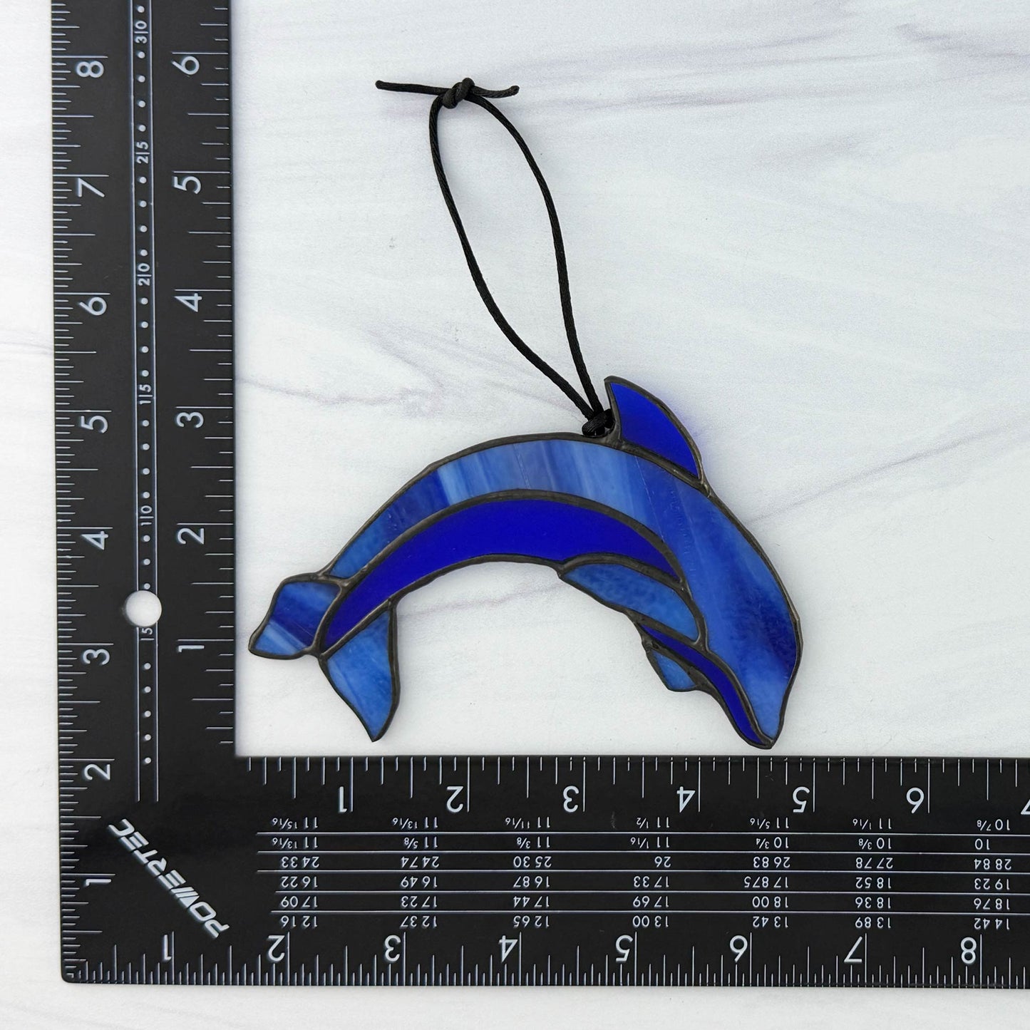 Stained glass dolphin ornament next to a ruler on a white background