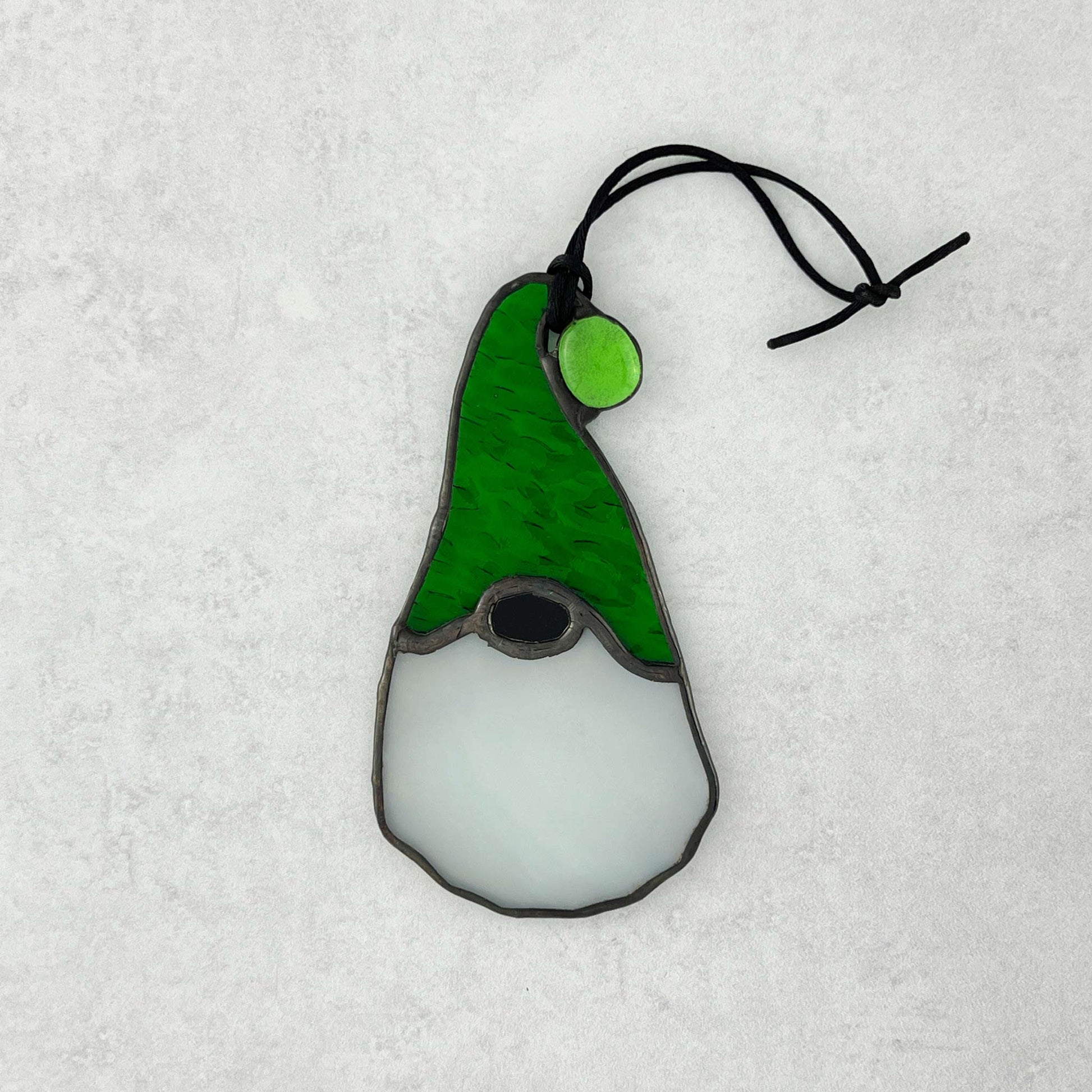 Stained glass gnome ornament with green hat and white body on a light gray background