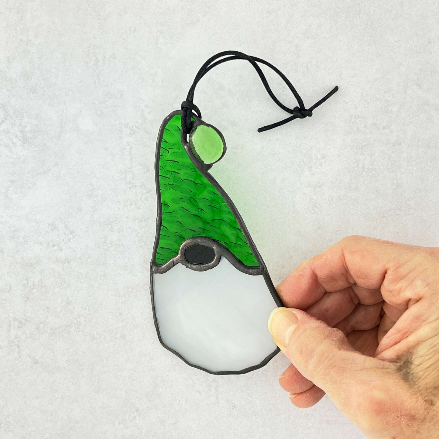 Hand holding a glass ornament gnome with a green hat on a light gray background