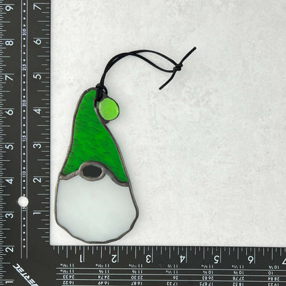 Stained glass gnome ornament with green hat and white beard on a white background with ruler for scale.