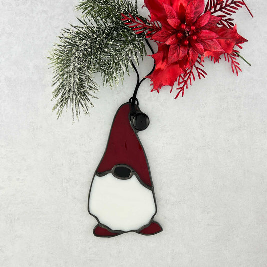 Stained glass gnome ornament with red hat and white body, hanging on a branch with red flowers.