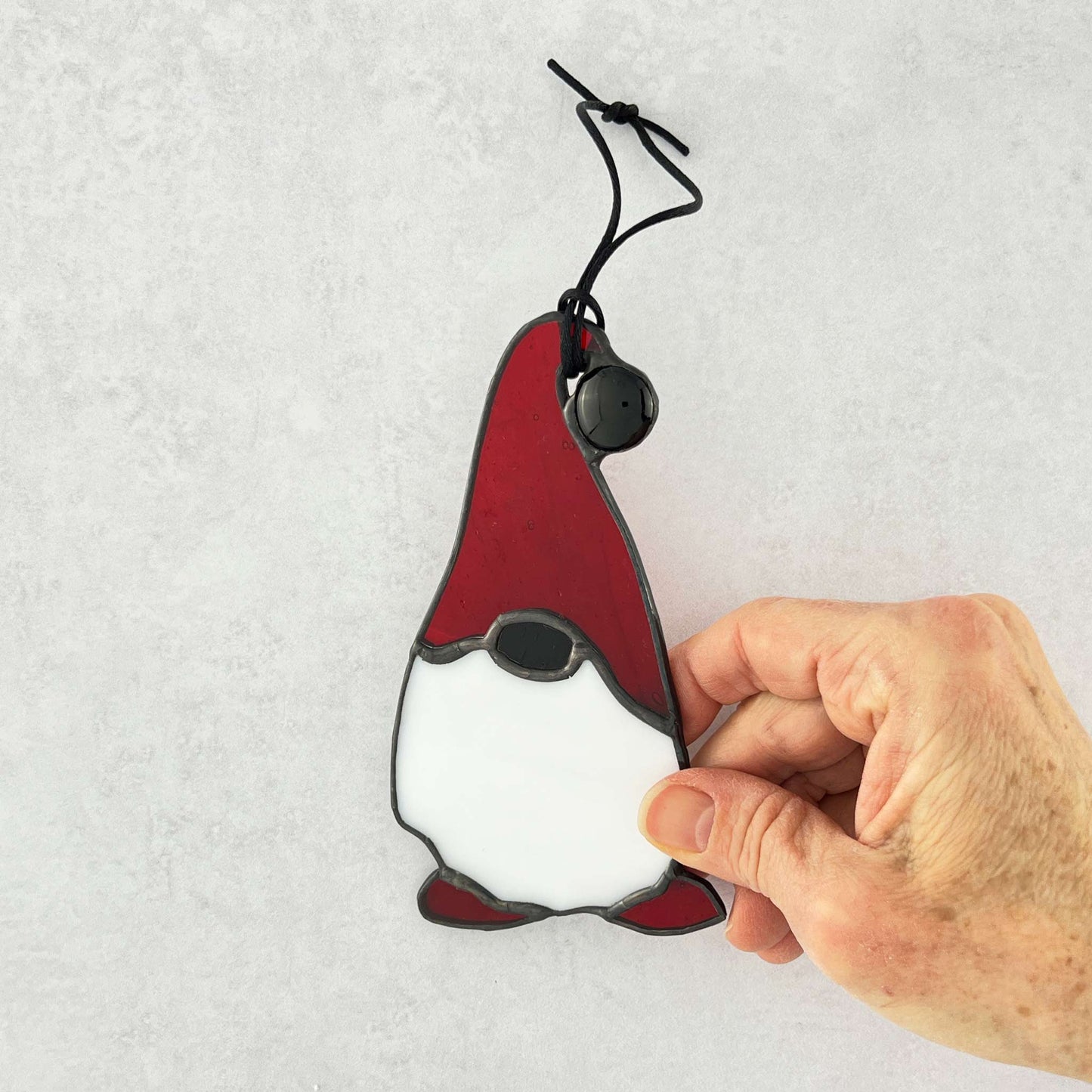 Hand holding a red and white gnome-shaped ornament against a light gray background