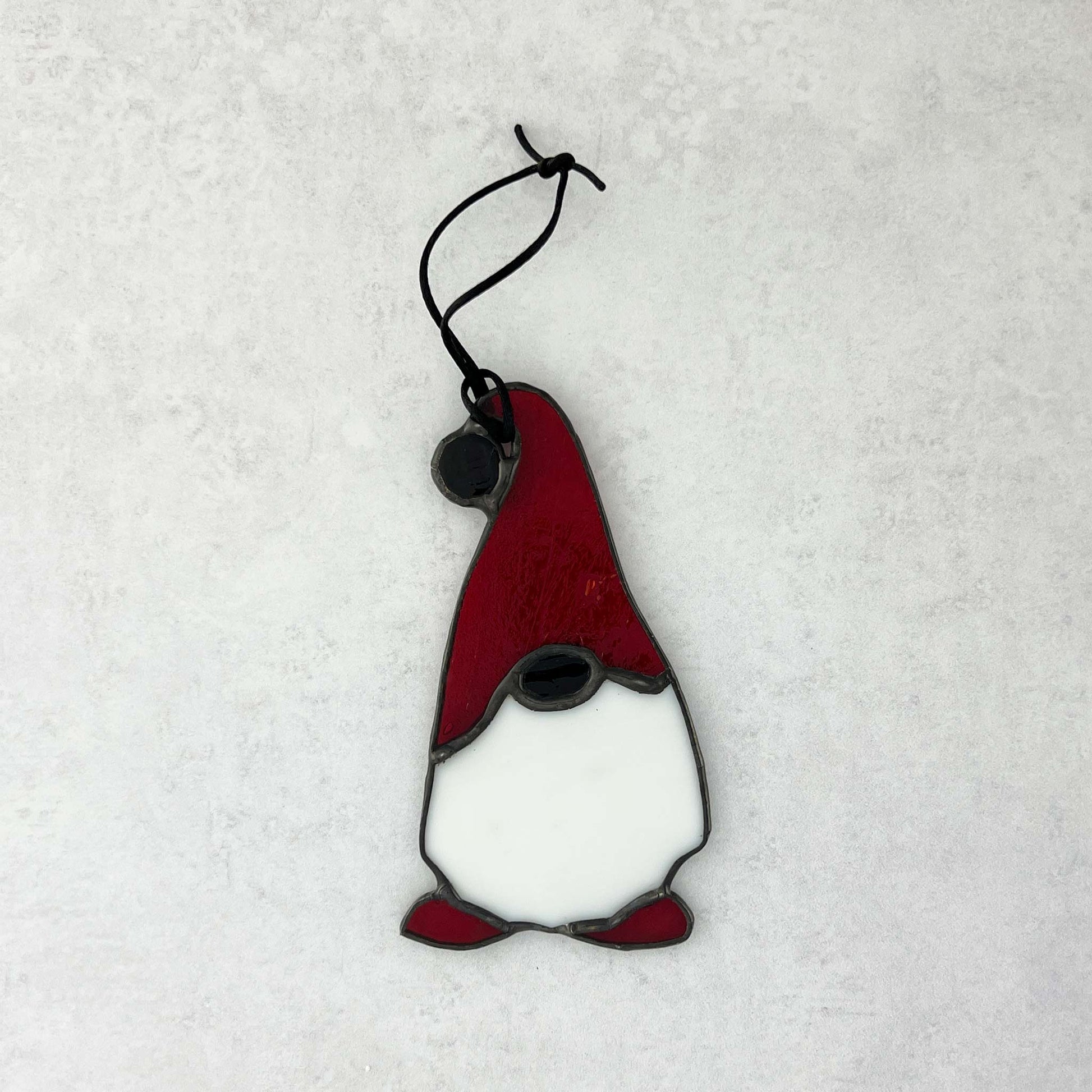 Stained glass gnome ornament with red hat and white beard on a light gray background