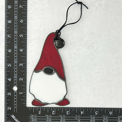 Stained glass gnome ornament with red hat and shoes on a white background with ruler for scale.
