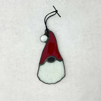 Stained glass gnome ornament with red hat and white beard on a textured white background. The hat has a white ball at the end.